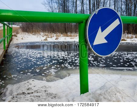 Thin ice in river near bridge with warning sign