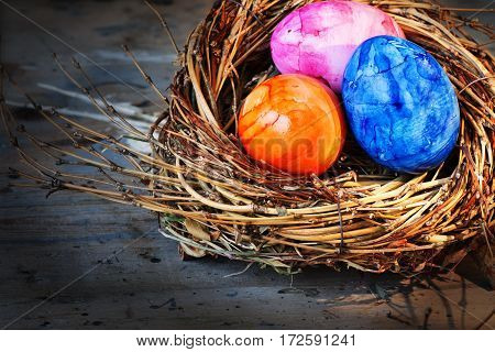 Easter eggs in radiant colors in a nest on an old shabby wooden table