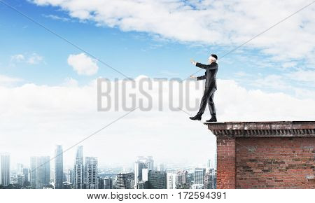 Businessman with blindfolder on eyes walking on building top