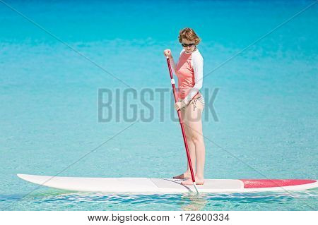 young woman in rashguard enjoying stand up paddleboarding at beautiful caribbean lagoon active vacation concept