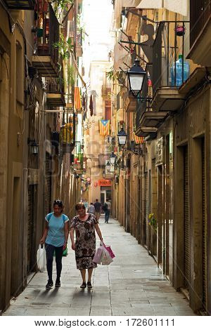 BARCELONA/ SPAIN - SEPTEMBER 29. Women with shopping bags walking on a narrow street in old district La Ribera on September 29, 2014 in Barcelona, Spain.