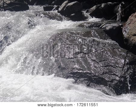 Water flowing over a large black rock. Black and white.