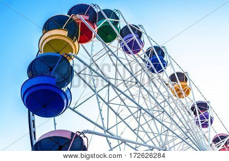 old Ferris wheel with colored cabins open against the blue sky