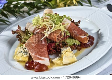meat salad with ham cheese lettuce Dorblu grapes and olive oil served on a plate on a table with flowers
