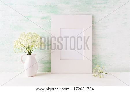 Easy white frame mockup with tender wild flowers in pitcher. Empty frame mock up for presentation artwork.