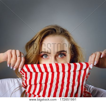 portrait of young female with surprised face holding scarf with white and red stripes. shot with copy space above head