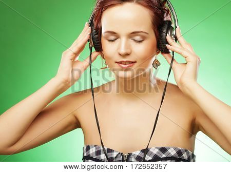 Young happy woman listening to music with headhones over green background