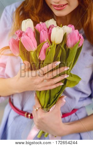 Two hands with rings holding bouquet of pink and white tulips