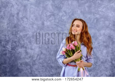 portrait of pretty female holding bouquet of tulips on the blue wall background. Wide shot with copy space