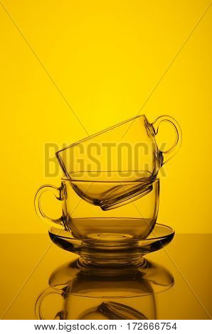Two transparent glass cups on yellow background