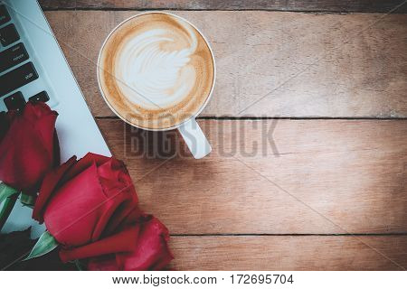 Red roses laptop computer and cup of coffee on wooden background with copy space.Valentines Day background concept Wedding day.Top view vintage tone