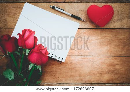 Red roses leather notebook pen and heart on wooden background with copy space.Valentines Day background concept Wedding day.Top view vintage tone