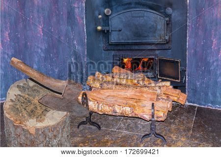 Interior fireplace in a corner with firewood and ax in an old country house