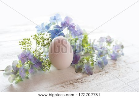 Easter decoration with flowers and a pink egg on a white wooden table