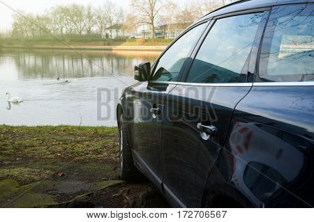 Detail of blue car parked in front of a lake with elegant swans on the blue surface