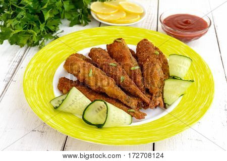 Deep frying small fish capelin on a plate on white wooden background.