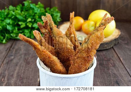 Deep frying small fish capelin in a mug on a dark wooden background. Good snack to beer.