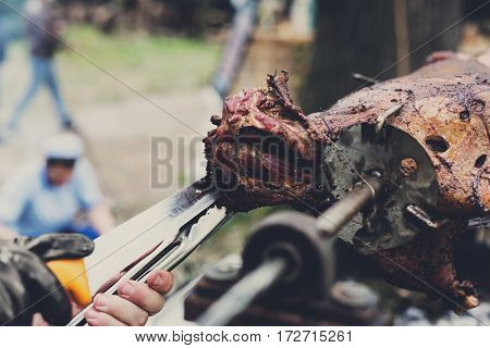 Barbecue picnic at country fair. Lamb roasted at spit closeup. Grill, big piece of meat at rolling skewer. Street vendor, professional chef hands cooking bbq food. Catering concept, vertical