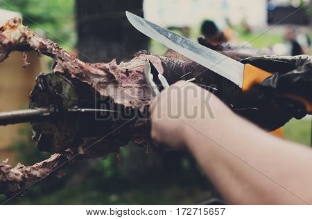 Barbecue picnic at country fair. Lamb roasted at spit. Grill, big piece of meat at rolling skewer. Street vendor, professional chef hands cooking bbq food, unrecognizable. Catering concept