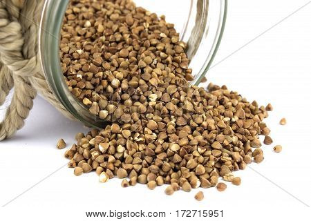 Buckwheat groats spilling out of glass jar on background