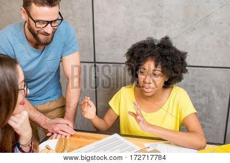 Multi ethnic coworkers dressed casually in colorful clothes talking together sitting with laptop indoors