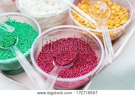 Ice cream treats and toppings sale. Rainbow sprinkles, stars, non pareil and glitter cupcake decorations, bright pink and green. Closeup in plastic plates with spoons. Confectionery store