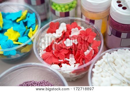 Ice cream treats and toppings sale. Rainbow sprinkles, stars, non pareil and glitter cupcake decorations, bright red and white. Closeup in plastic plates with spoons. Confectionery store