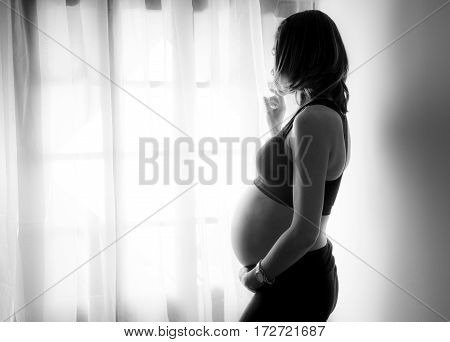 Pregnant woman looks at the street through the window