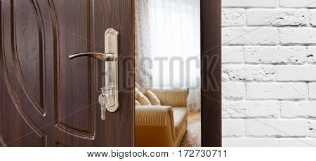 Half opened door handle closeup, entrance to a living room, sofa and window. Welcome, privacy concept. Door lock with keys, white brick wall, modern interior design.
