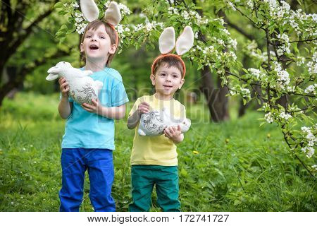 Two Little Kids Boys And Friends In Easter Bunny Ears During Traditional Egg Hunt In Spring Garden,