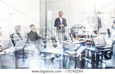 Successful team leader and business owner leading informal in-house business meeting. Business people working on laptops in foreground and glass reflections. Business and entrepreneurship concept.