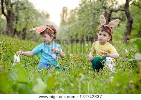 Two Little Kids Boys And Friends In Easter Bunny Ears During Traditional Egg Hunt In Spring Garden,