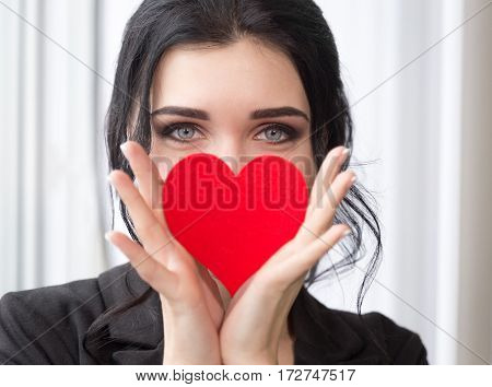 Beautiful caucasian girl holding red heart cover her face. Shallow depth of field. Valentine day concept.