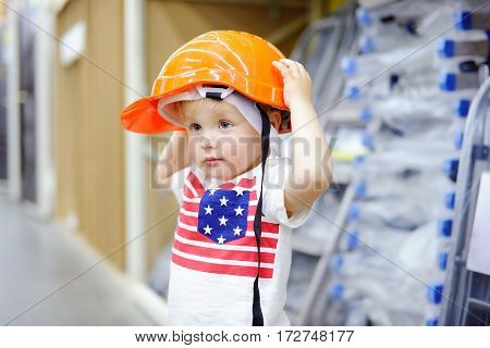 Little boy having fun in a hardware store. Toddler builder choosing the right helmet in a hardware store. Childhood concept