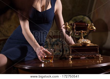 Female hand holding a glass of whiskey near the retro dial phone