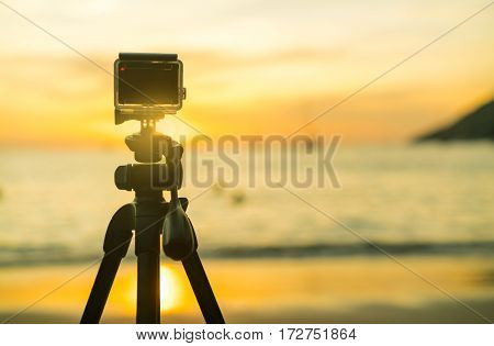 Action compact camera on a tripod to take photos and video of people on the beach during sunset.