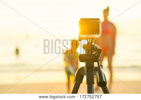 Action compact camera on a tripod to take photos and video of people on the beach during sunset.