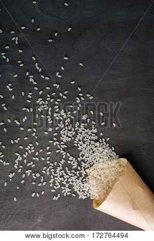 White Rice Scattered Over The Dark Wooden Table Of A Paper Bag.