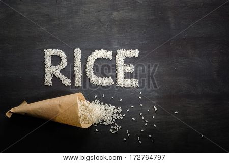 White Rice Scattered Over The Dark Wooden Table Of A Paper Bag.