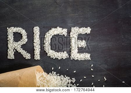 White Rice Scattered Over The Dark Wooden Table Of A Paper Bag.