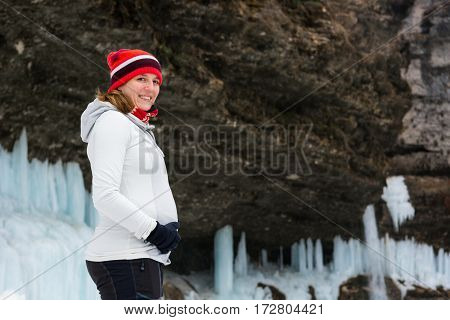 Young pregnant woman smiling on winter landscape. Icicles and snow in the background.