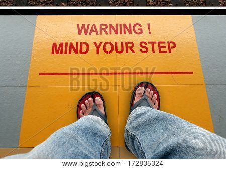 Mind your step signage on a train platform with a man standing
