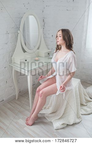Gorgeous woman in erotic lingerie sitting on a chair in a bright room.