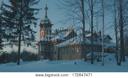 Beautiful traditional snow-covered russian cottage - terem surrounded by a forest and evergreen fir tree near it.