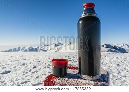 Vacuum Flask Of Hot Tea On A Table With A Boundary Marker In The Winter In The Mountains.