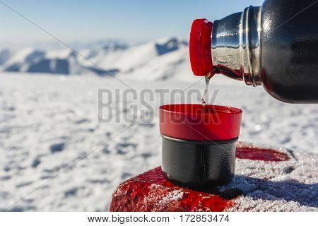 Pouring hot tea from a thermos into a cup in the winter in the mountains.
