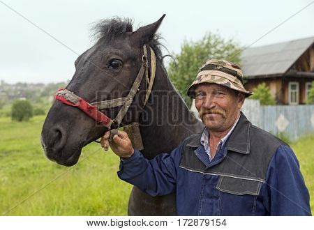 An elderly farmer with his horse in the rain. Old-believer village Visim, Russia.