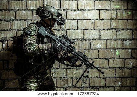 US Army Ranger member with machinegun and night vision goggles moving along the wall during mission