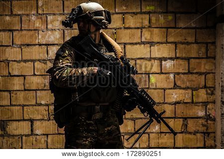 US Army Ranger with machinegun and night vision goggles standing near the wall. Side view profile