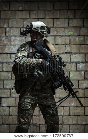 US Army Ranger with machinegun and night vision goggles standing near the wall. Side view profile